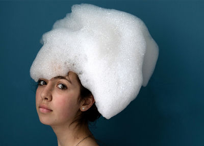 Portrait of young woman wearing hat standing against blue background