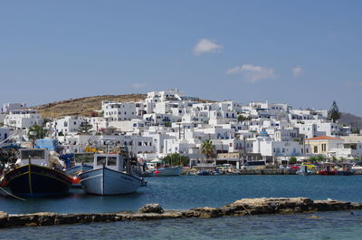 Boats moored in sea by town against sky