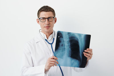 Portrait of doctor holding stethoscope against white background