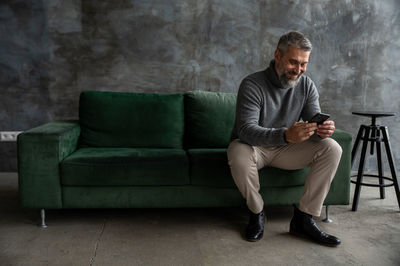 Full length of young man sitting on sofa at home