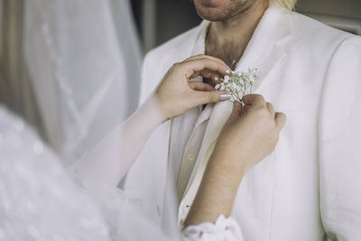 Midsection of bride adjusting boutonniere in groom's pocket on wedding