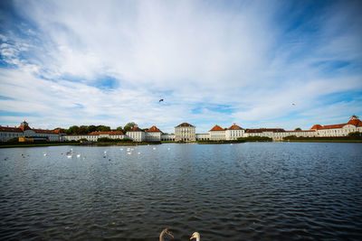 Birds flying over lake and buildings against sky