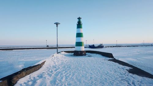 Lighthouse by frozen sea against clear sky