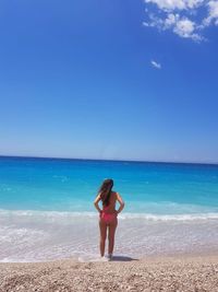 Full length of woman standing on beach against blue sky