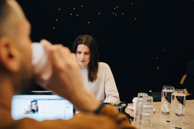 Male programmer drinking coffee while confident young female hacker working at desk in small office