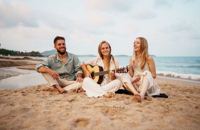 Friends sitting at beach against sky