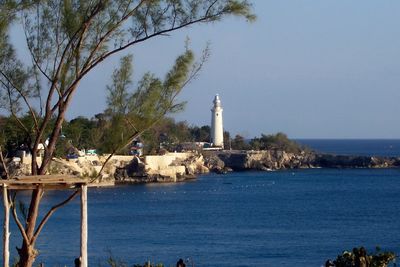 Lighthouse by sea against clear sky