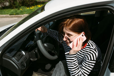 Portrait of a young brunette woman driving in a car using a smartphone