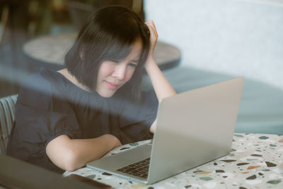 Woman with head in hands wearing while mask sitting by laptop on table