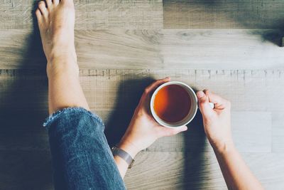 Low section of woman holding coffee cup on floor