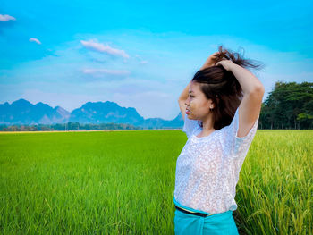 Happy young woman standing on field against sky