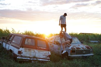 Man standing by car on field against sky during sunset