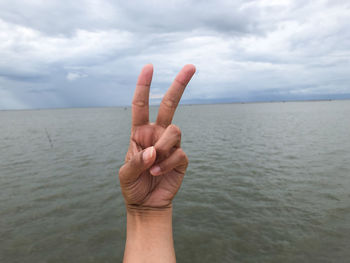 Midsection of person hand in sea against sky