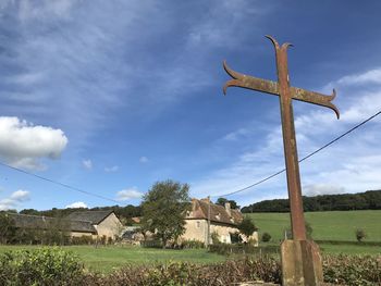 Cross on field by building against sky