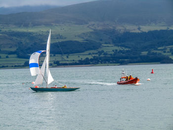 Sailboat sailing on sea against mountains