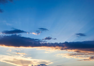 Low angle view of sunlight streaming through clouds