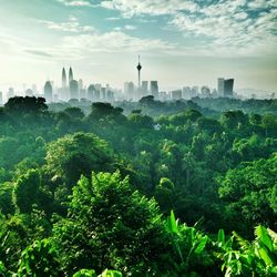 Menara kuala lumpur tower amidst buildings in front of trees against sky