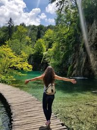 Rear view of woman standing by lake against trees