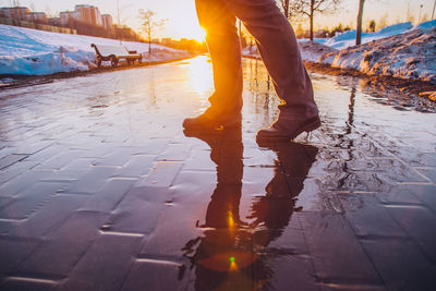 Low section of man standing on puddle during sunset