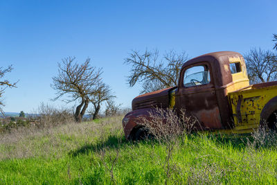 Abandoned truck on field against clear blue sky