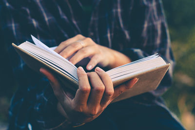 Midsection of woman reading book while sitting outdoors