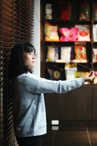 Side view of young woman standing against window at home