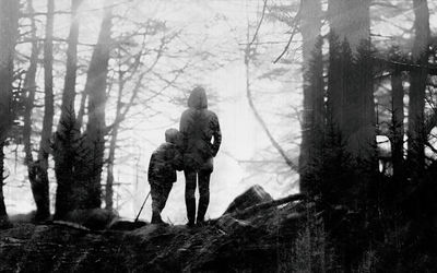 Rear view of mother and child standing on field amidst trees