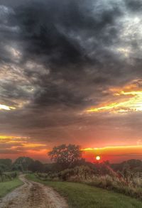 Scenic view of landscape against cloudy sky at sunset