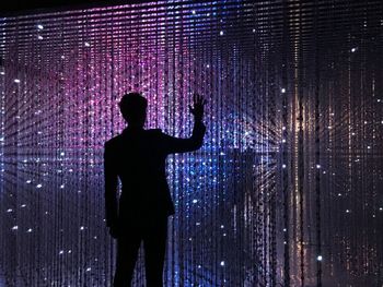 Rear view of silhouette man standing against illuminated light at night