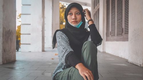 Portrait of young woman sitting on sidewalk in city