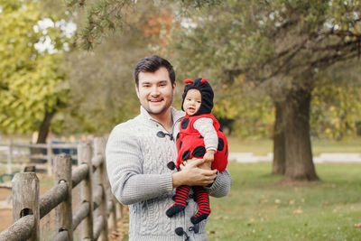 Portrait of smiling father carrying cute daughter while standing in park