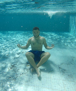 Full length of shirtless young man meditating in swimming pool