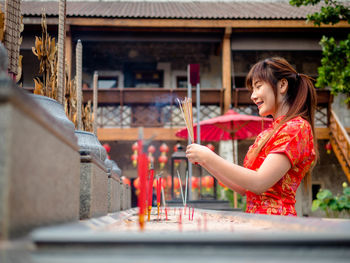 Side view of woman holding incense sticks against building