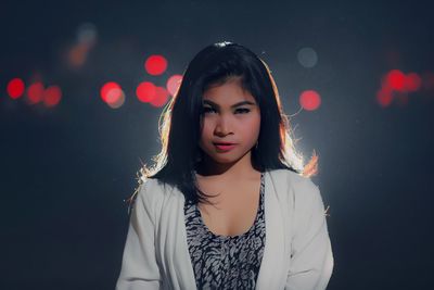 Portrait of beautiful young woman standing against illuminated light at night