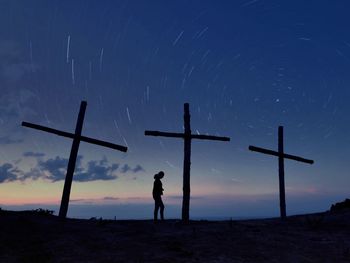 Silhouette woman standing by cross against star trail
