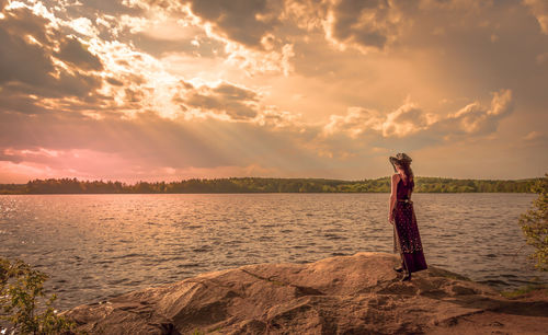 Woman standing in sea against sky during sunset