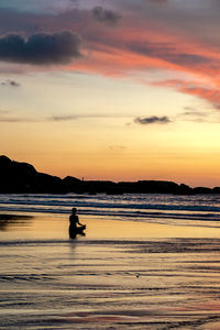 Silhouette person meditating at beach against sky during sunset