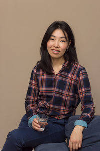 Portrait of smiling young woman sitting against wall