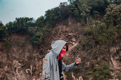 Side view of woman in hood and mask standing against mountain