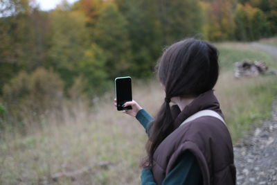 Rear view of woman photographing through mobile phone
