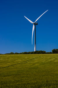 Windmill on field against clear blue sky