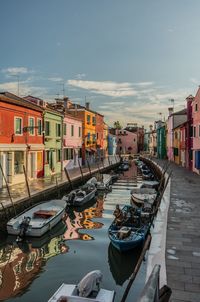 Boats moored in canal amidst buildings in city against sky