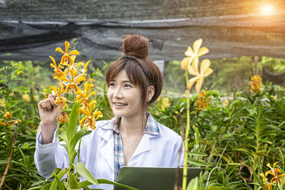 Smiling woman holding magnifying glass against flower