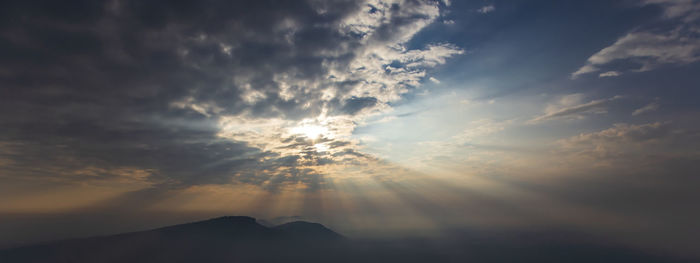 Low angle view of sunlight streaming through clouds during sunset