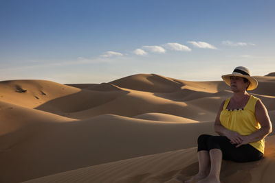 Man sitting on sand dune in desert against sky