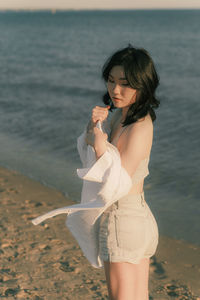 Young woman standing at beach during sunset, with white blouse
