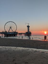 Ferris wheel on beach against clear sky at sunset