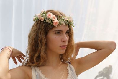 Close-up of thoughtful woman wearing flowers while standing against curtain