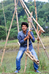 Full length portrait of young man sitting on bamboo over grass