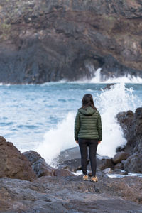 Rear view of woman standing on rock by sea